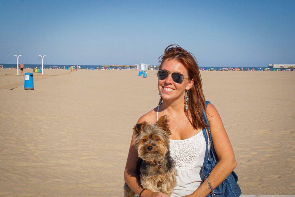 Woman holding a Yorkshire Terrier on a wide sandy beach in Barcelona